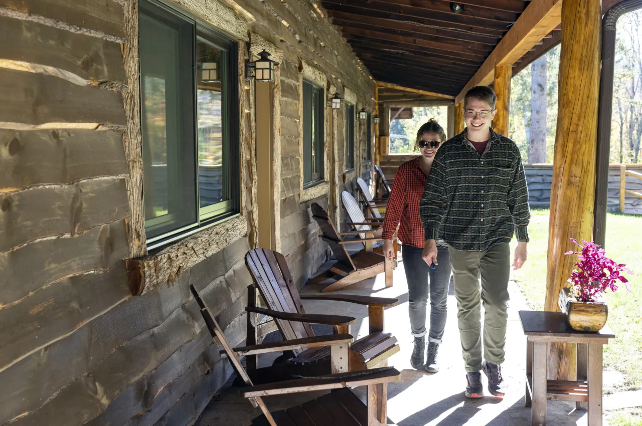 Young man and woman walk along covered porch past Adirondack chairs