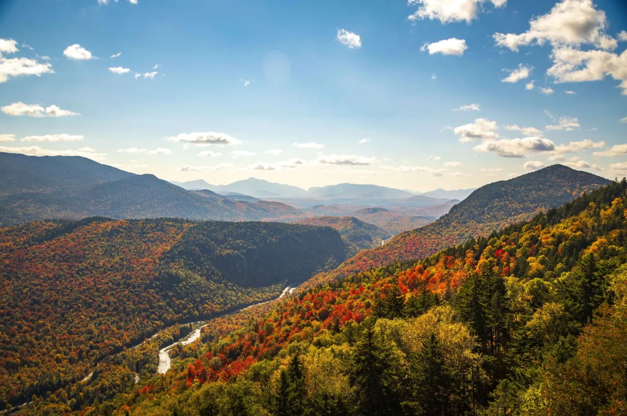 Scenic mountain landscape with bright fall foliage reds and oranges and a lightly cloudy sky