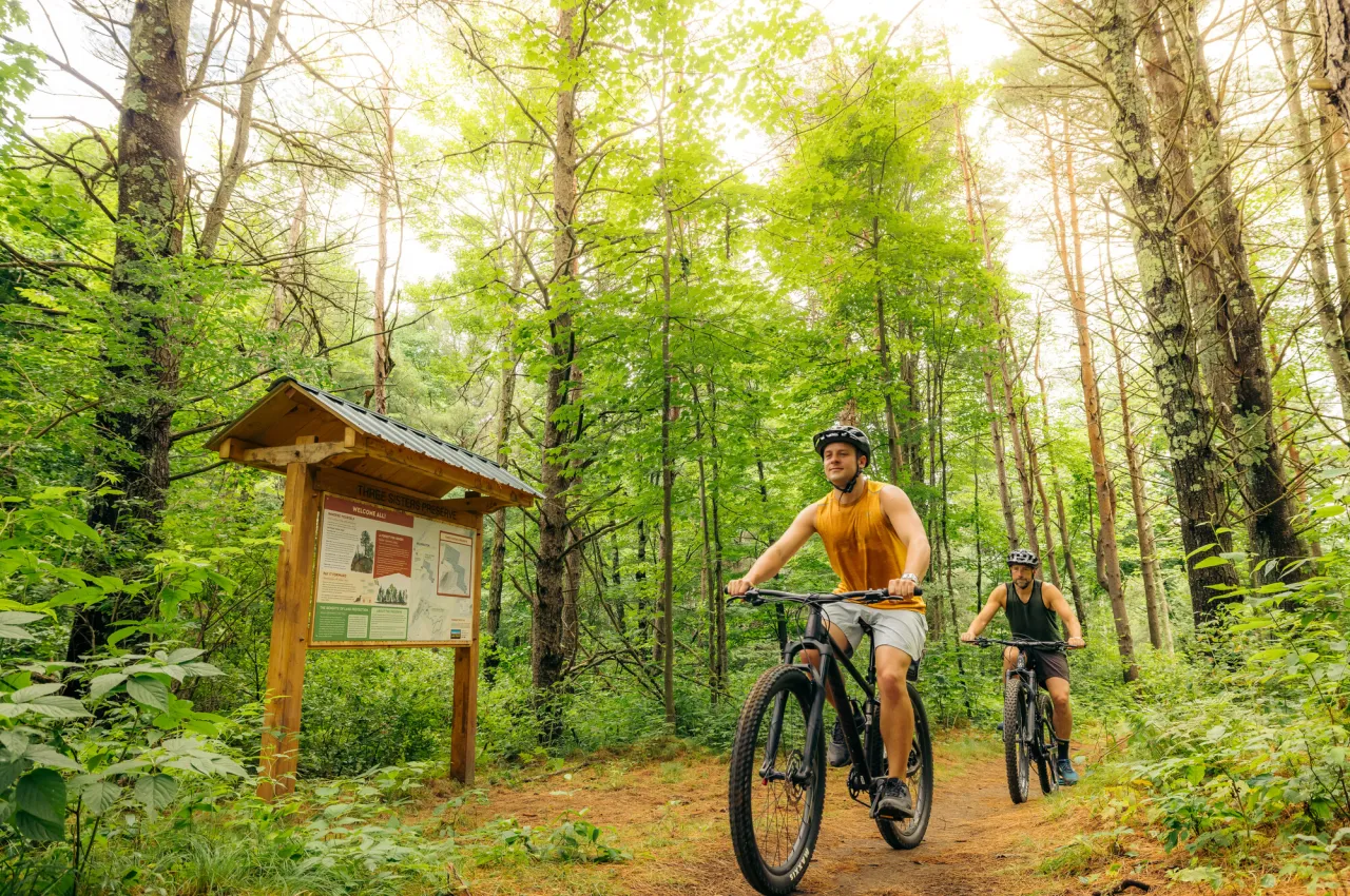 Two mountain bikers at the start of a forested trail