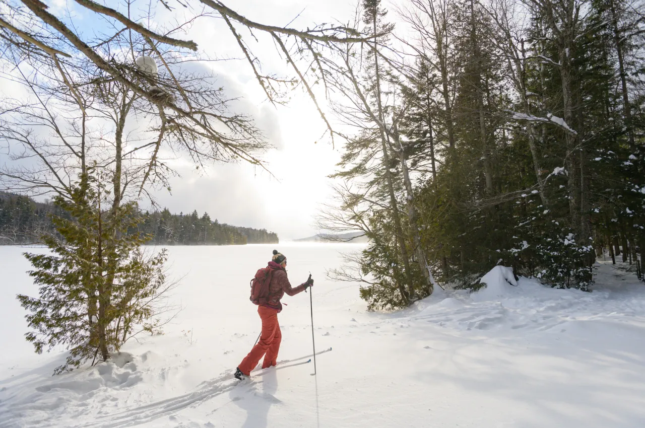 Person in red snow pants snowshoes past frozen winter pond