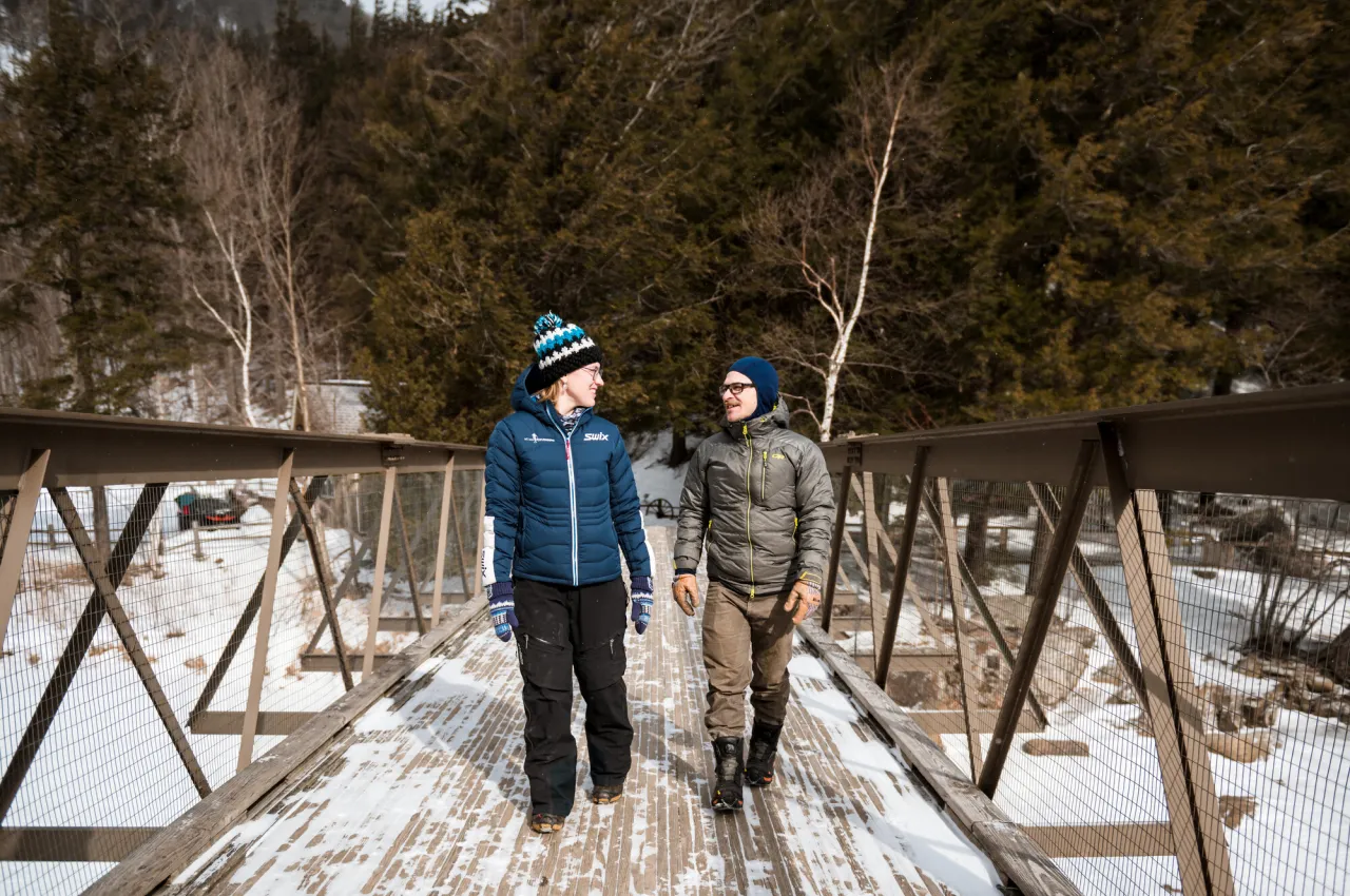 Man and woman in winter clothing walk across snowy bridge looking at each other