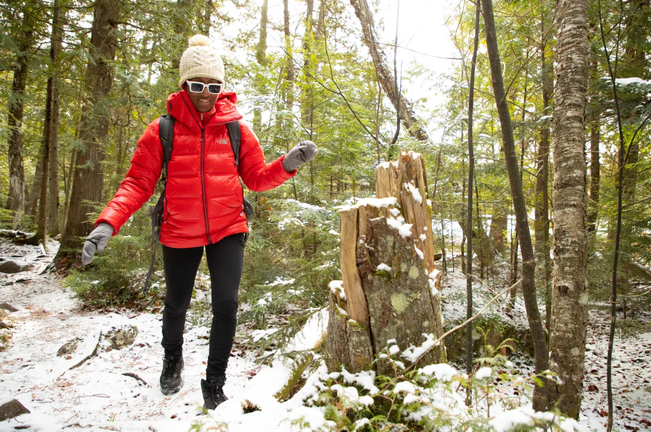 Woman in red coat and white hat walks on snowy forest trail