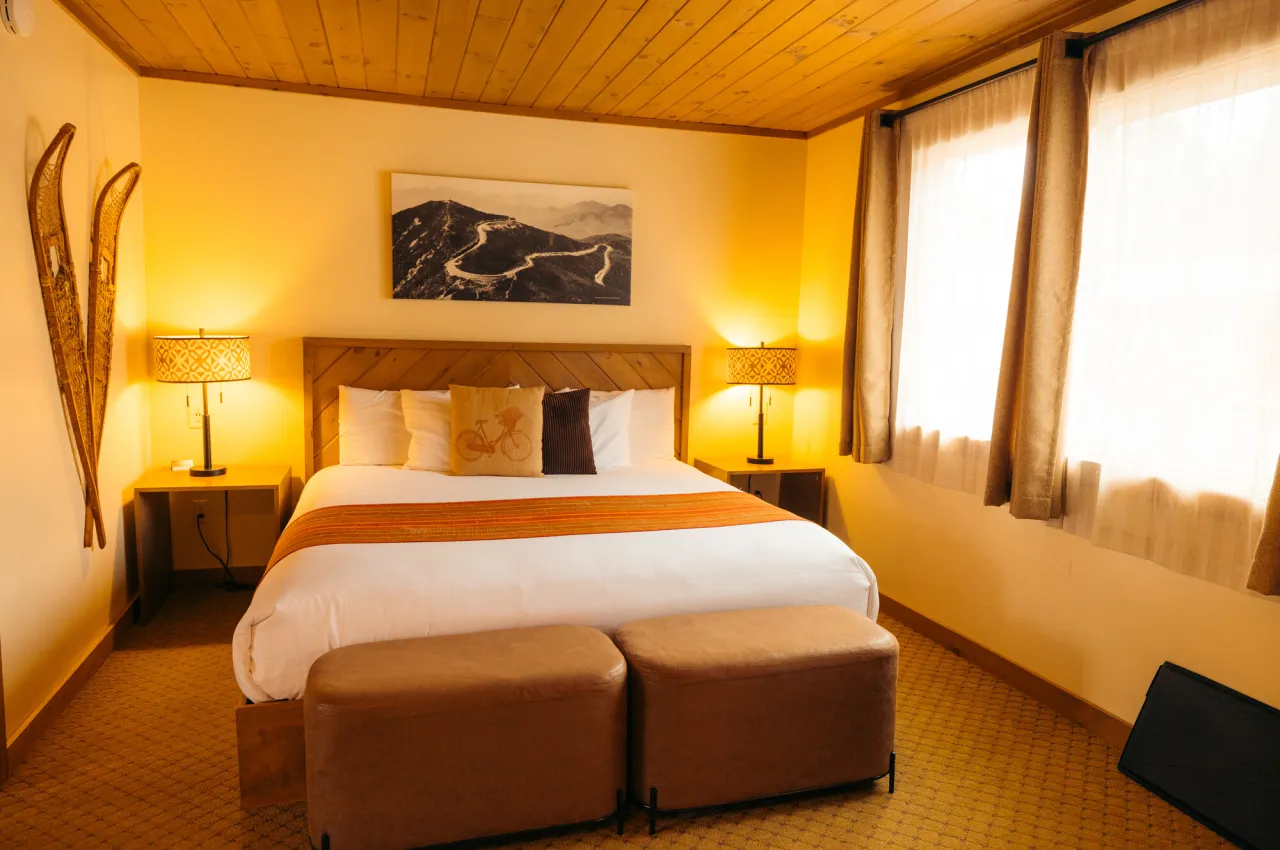 Queen bed in warmly lit room with snowshoes on one wall and windows on the other