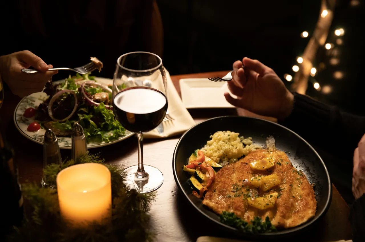 Trout dish, red wine, and salad on table lit by candle