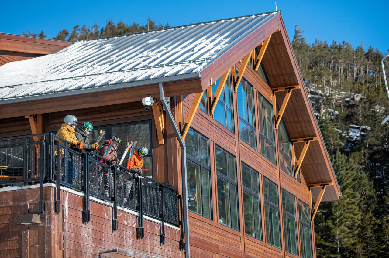 Four skiers look out from balcony at lodge