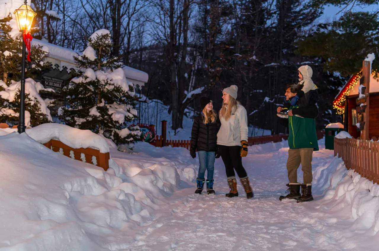 Family of four stands on snowy walkway with smallest child on father's shoulders