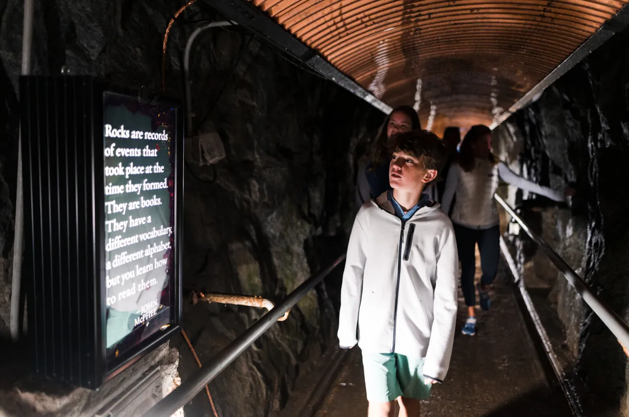 Boy walks through dark tunnel looking at lit sign