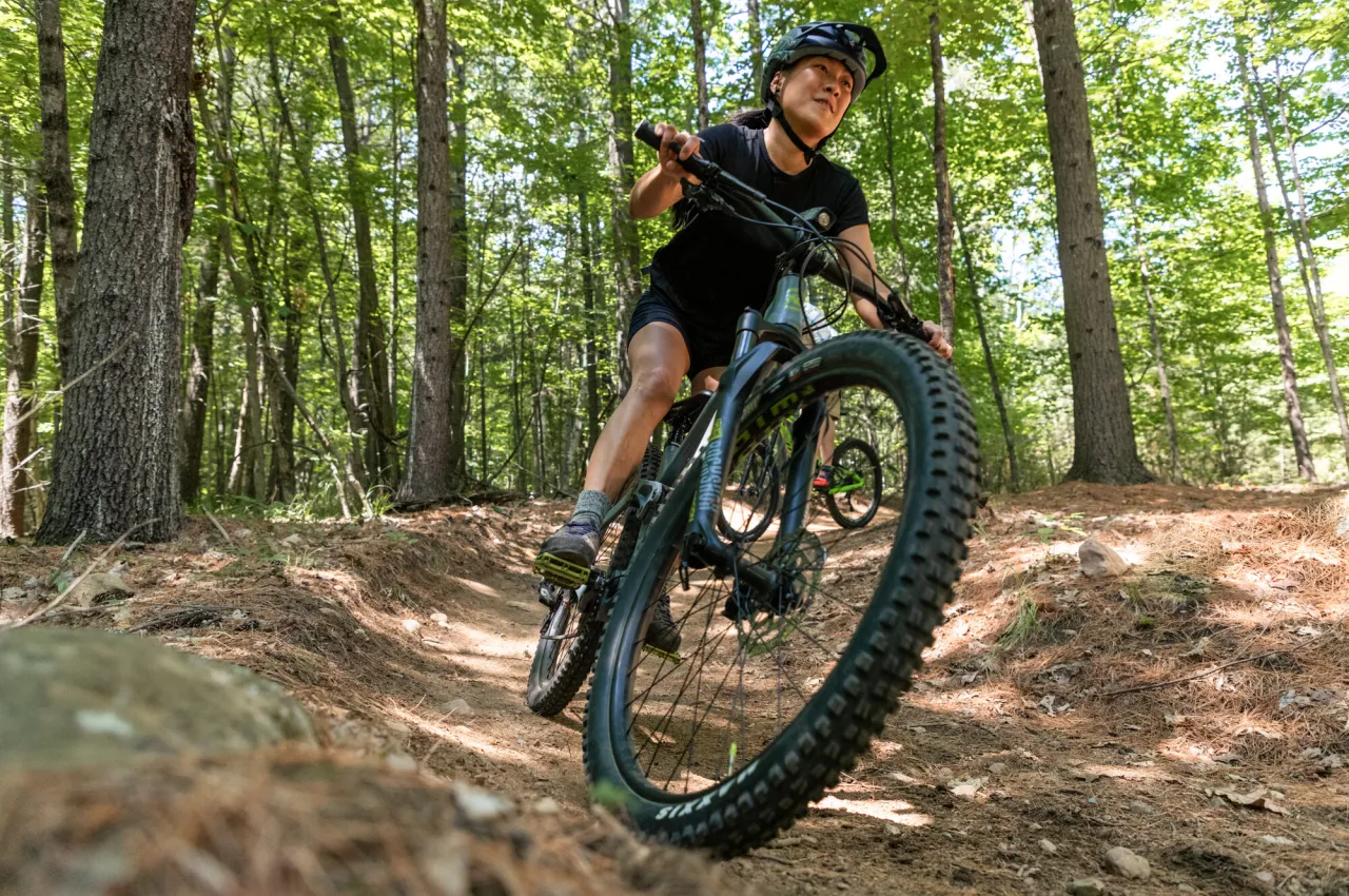 Woman in black t-shirt and shorts wearing a helmet rides a mountain bike on a wooded trail