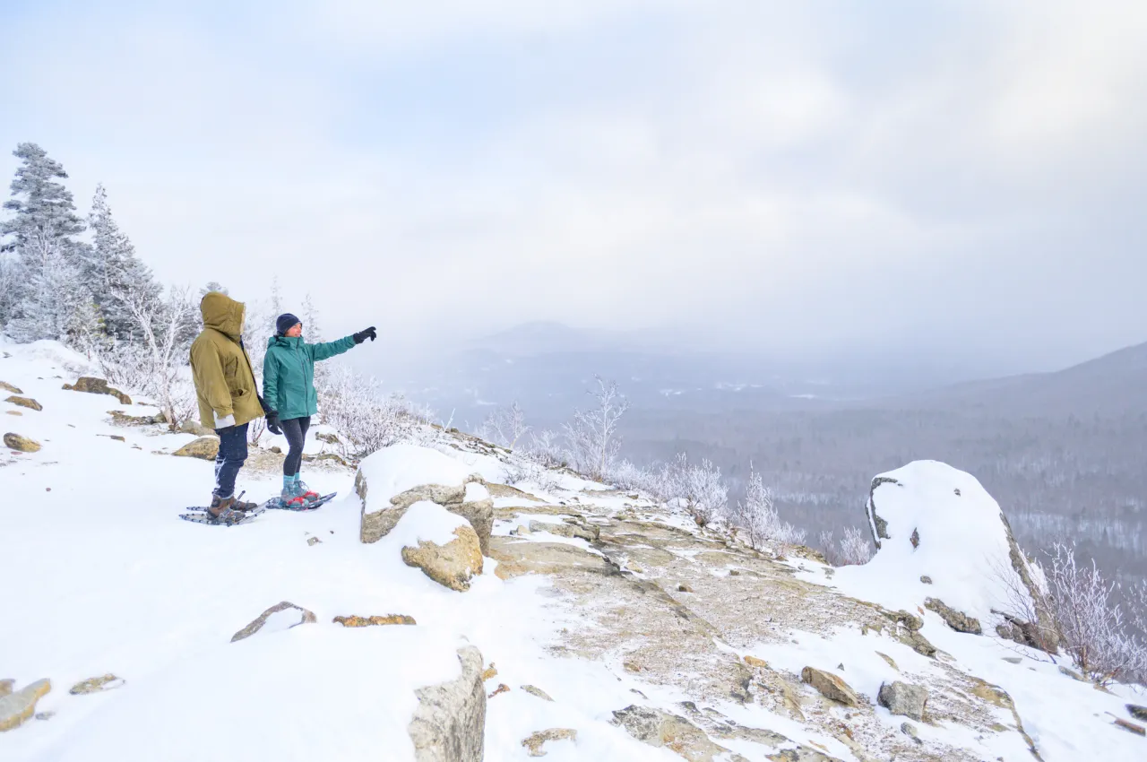 Two hikers take in the wide open space on top of a mountain in the Whiteface region