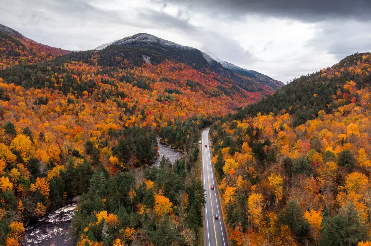 a fall mountain scene with cars driving down a road. 