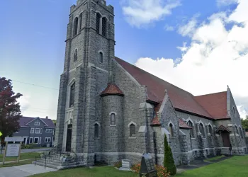 Ground level view of the exterior of the impressive gothic style  church entrance made of grey stones with white stone trim around the windows and a red roof.