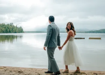 A bride and groom walk the sandy shores of Lake Champlain.