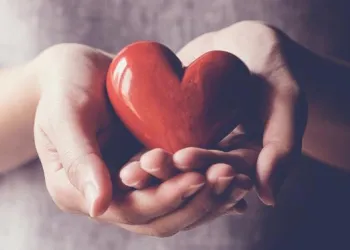 Hands holding a red heart shaped polished stone.