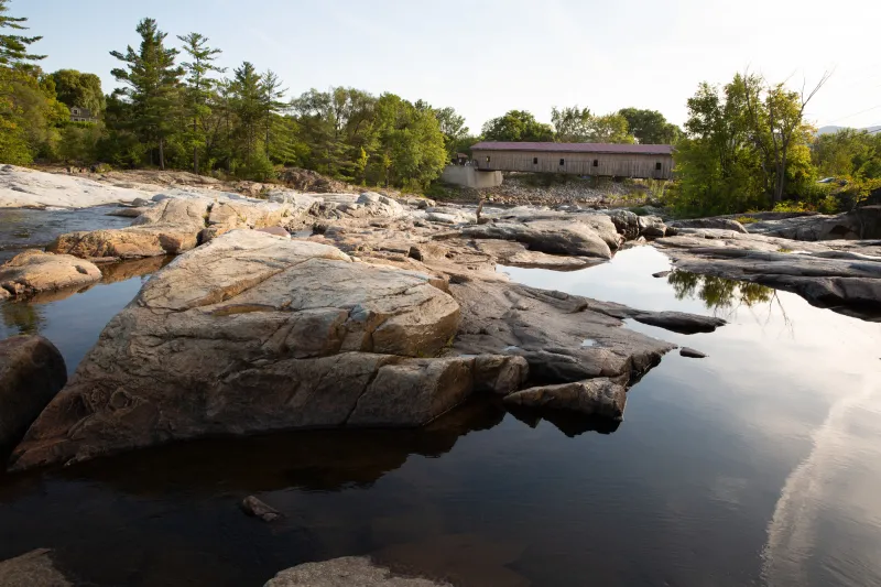 A rocky stream with a covered bridge in the distance.