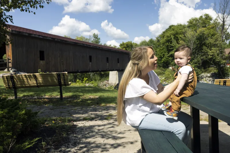 A woman holds her baby at a picnic table.
