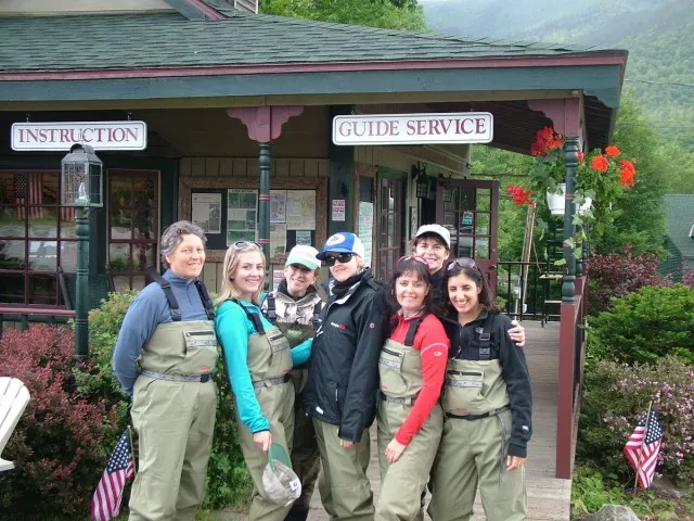 A group of women in fishing waders in front of a fly fishing guide shop.