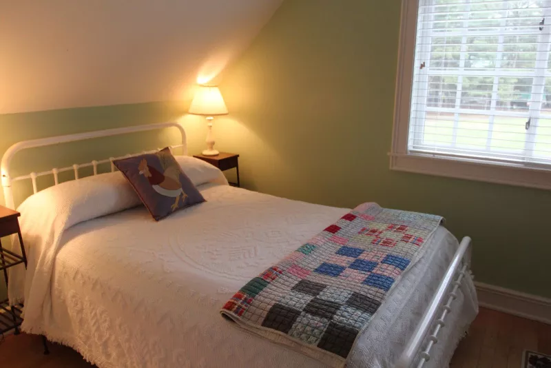 A bed with a rooster-decorated pillow and white sheets inside a bedroom