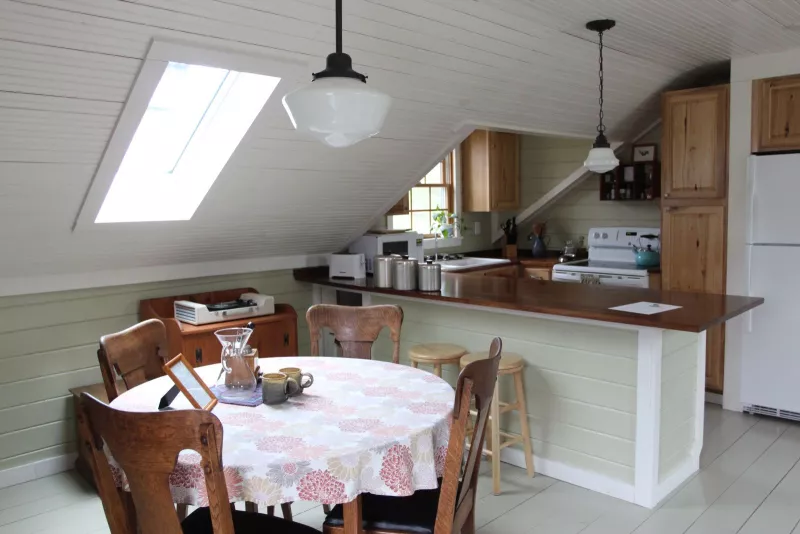 A round table with a pink tablecloth surrounded by four chairs in a wooden and white tiled kitchenette