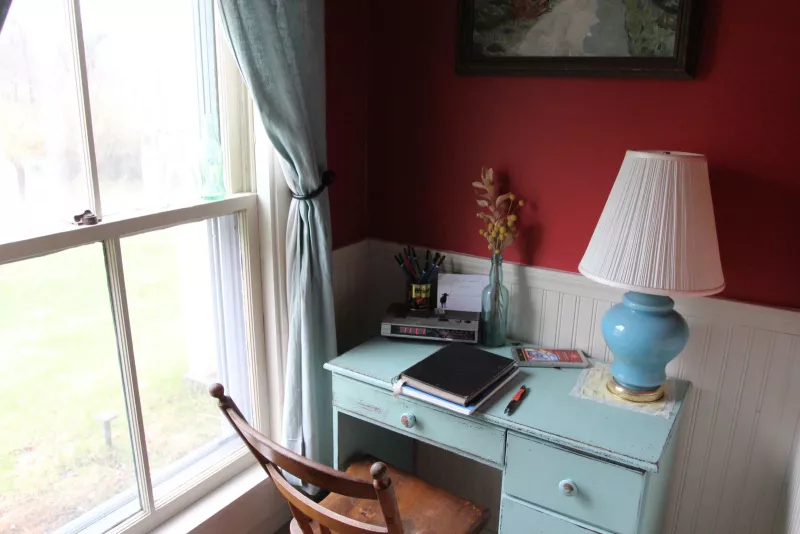 a black notebook sits on top of a light blue wooden small desk with a blue lamp and wooden chair