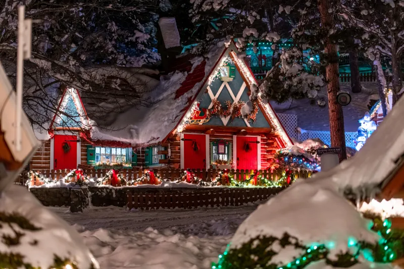 A colorful Alpine cottage is decorated with reindeer shutters, holiday lights, and an image of Santa.