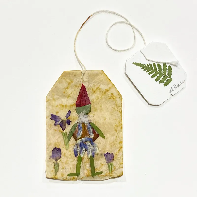 The artist reuses a tea bag as the background for her character, who is green and wears a red hat. The character is picking purple flowers. Photo by Alison Haas.