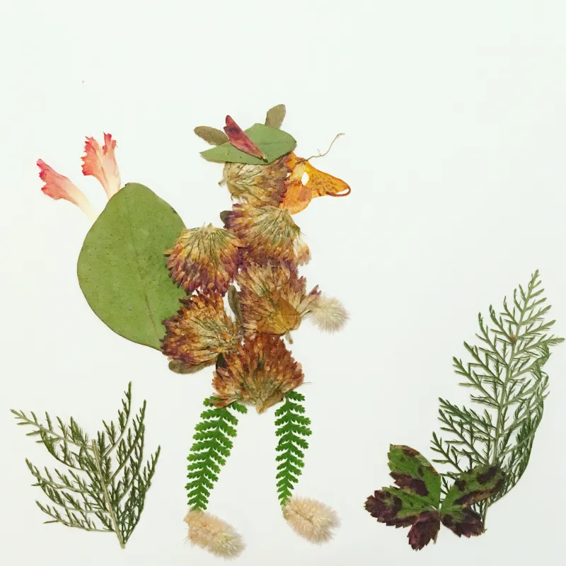 A wolf walking on his hind legs and wearing a big green backpack and green hat, all made of pressed flowers and leaves. Photo by Alison Haas.