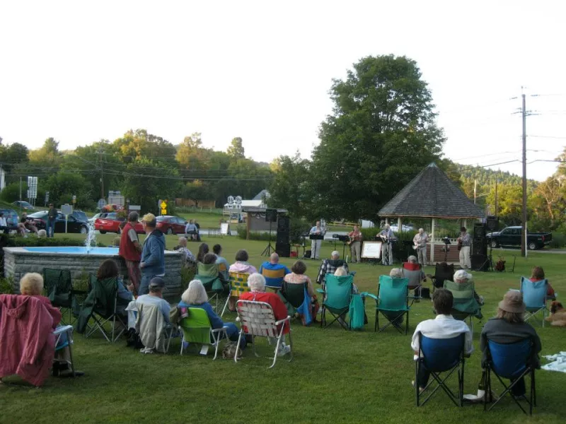A small crowd of people in lawn chairs enjoy a concert on the Jay, NY village green.