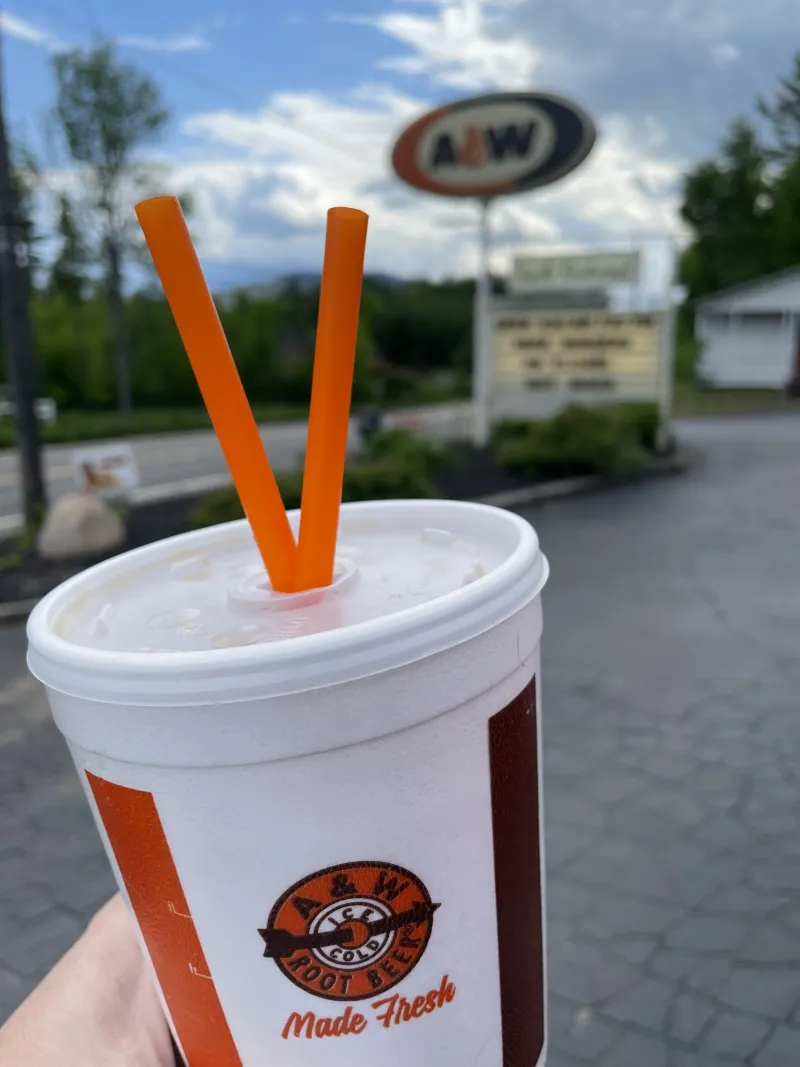 An A&W brand cup with two straws in front of the A&W sign.