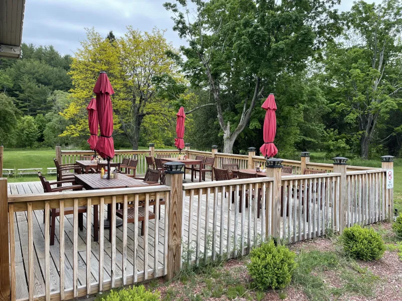 An outdoor dining deck with four tables and umbrellas and green scenery.