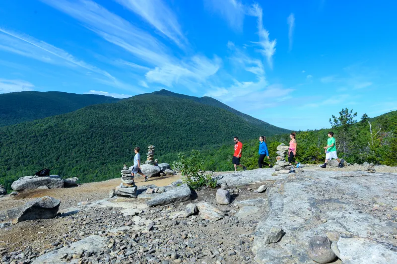 A family in colorful shirts walks on a mountain summit.