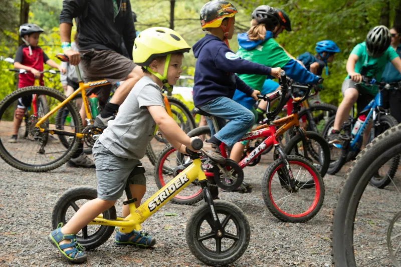 A large group of children gather together on their bikes and striders.