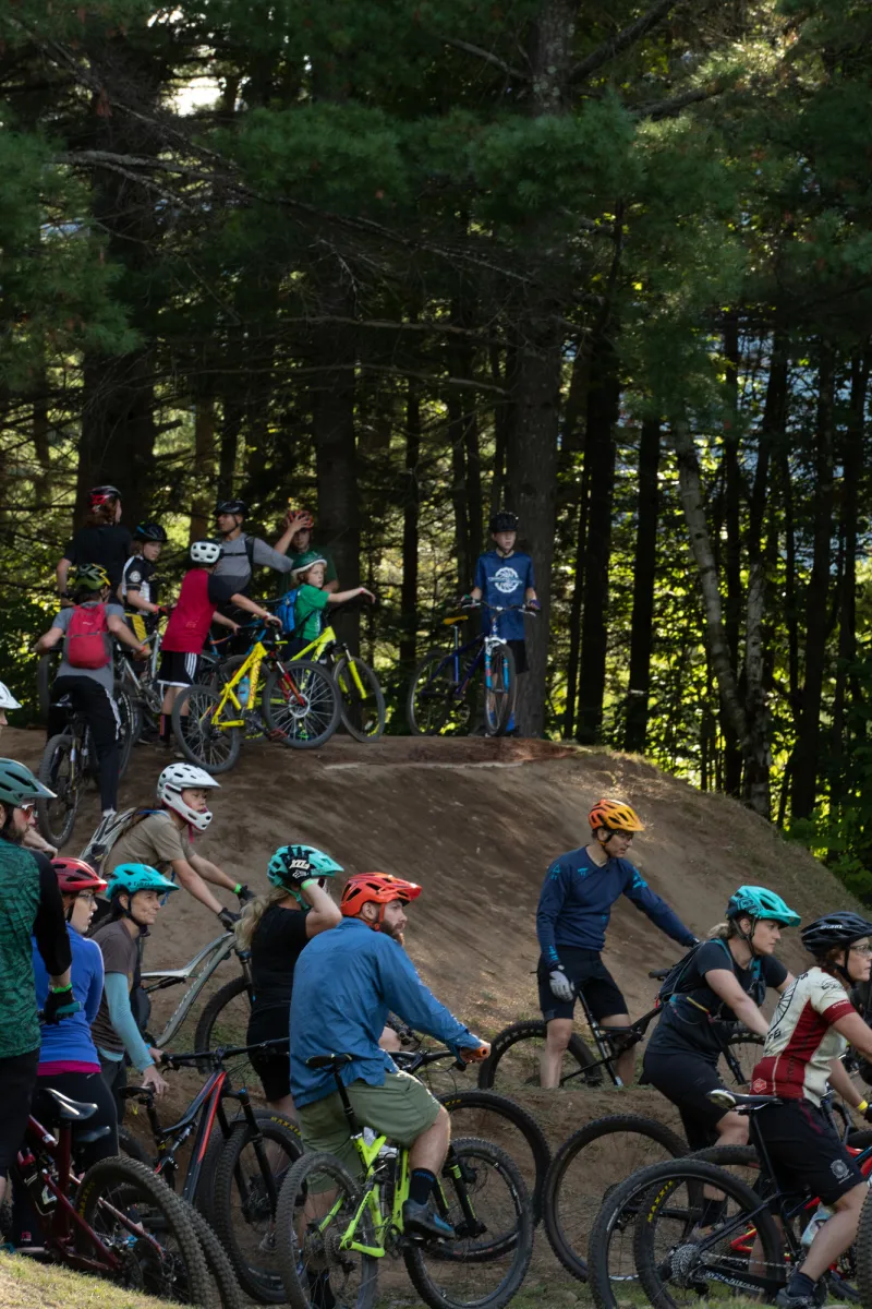 A group of mountain bikers gather on top of a hill to listen to a skills clinic.