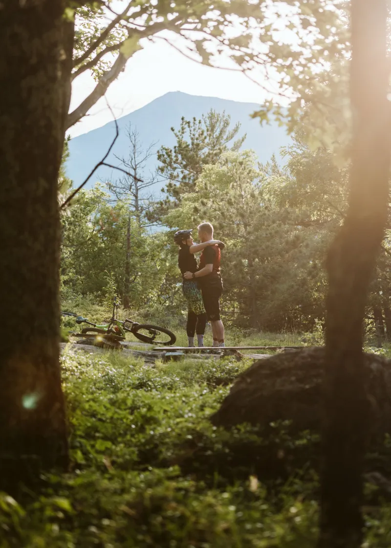 A man and woman embrace in the sunshine with mountains in the background