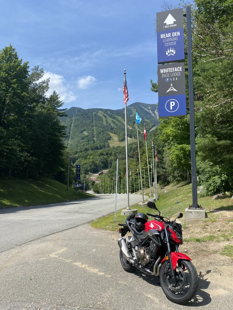 A red motorcyle sits in front of the steep backdrop of Whiteface Mountain in summer.
