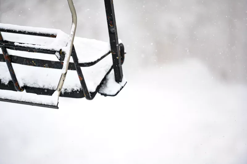 Snow built up on a stationary chair on a lift.