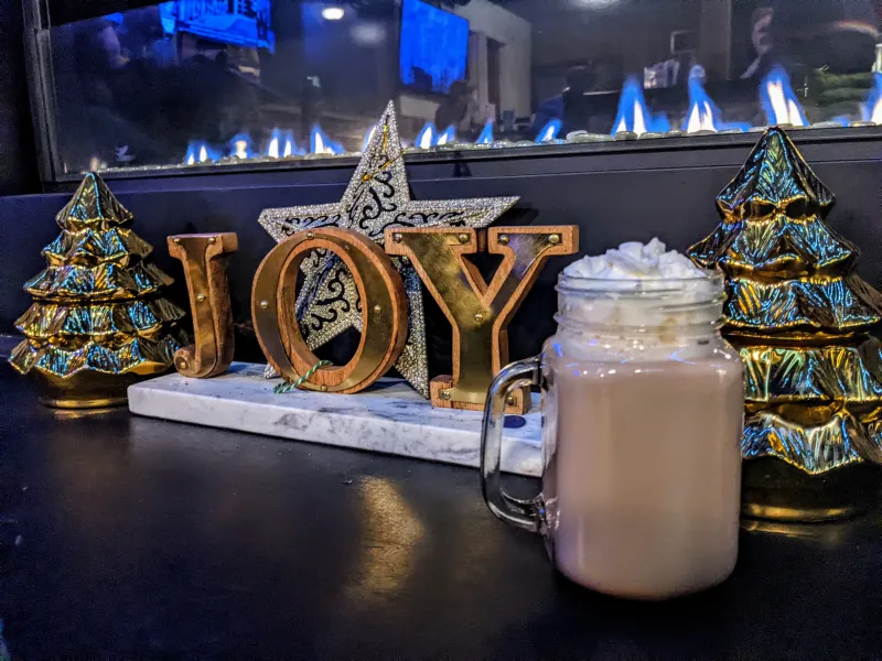 A mason jar of hot cocoa with whipped cream is placed in front of Christmas decorations.