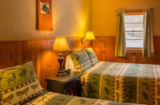A cozy motel room with two beds in Adirondack, rustic sheets.