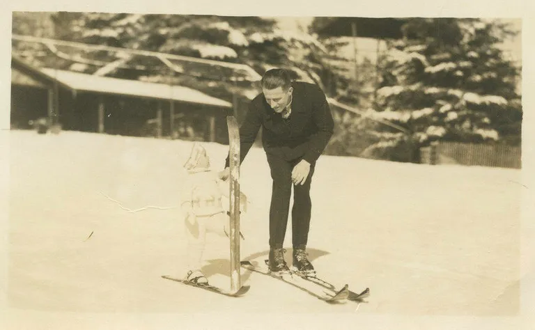 A vintage sepia-toned photo of a man and baby on skis.