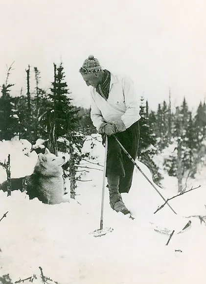 A vintage, black and white photo of a man on skis with a dog in the snow