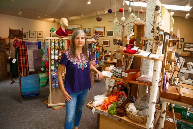 A woman stands in a showroom with a variety of art mediums and colorful yarn