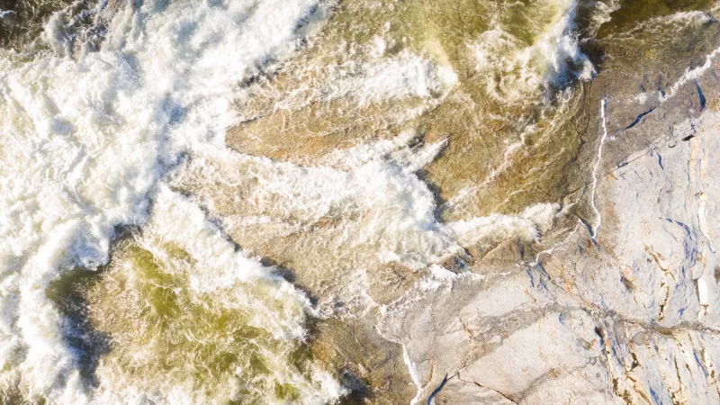 An aerial view of turbulent river waters on a rocky shoreline.