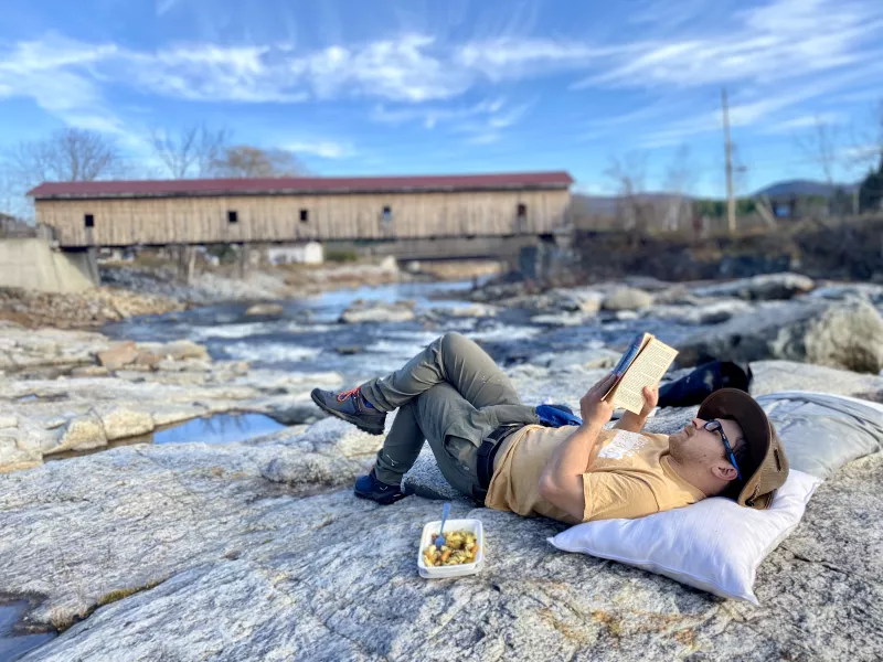 man sunbathing on rocks at covered bridge and reading a book