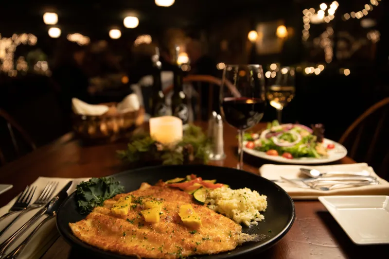 Dinner table full of food and drinks sits in front of a fireplace