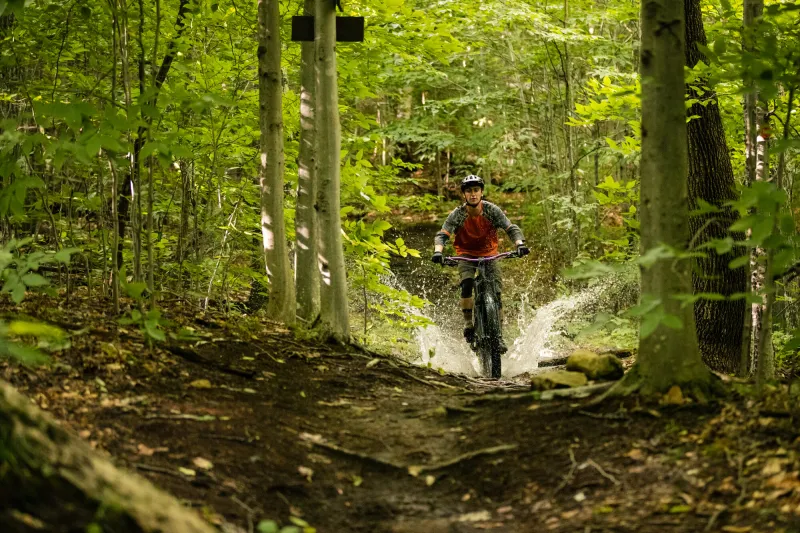 Mountain biker splashes through a puddle while riding on a trail through the woods
