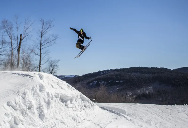 A skier jumping in the air and touching the back of their skis.