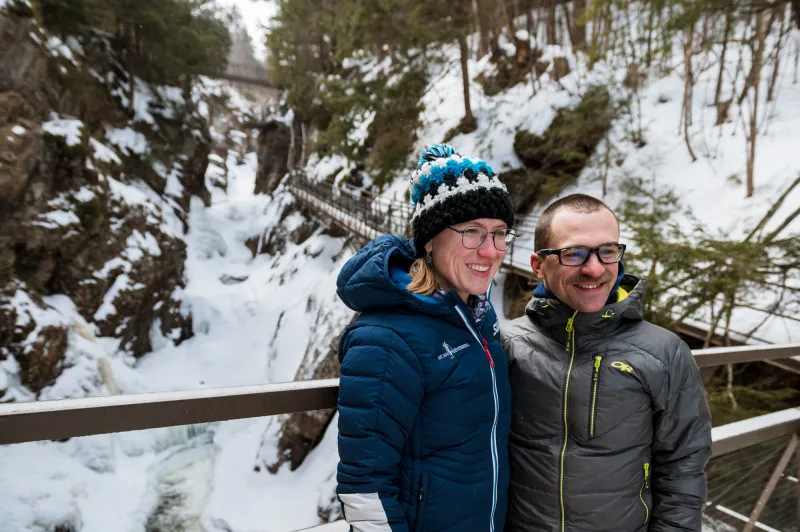 A man and woman smile for a photo in front of a snowy river gorge.