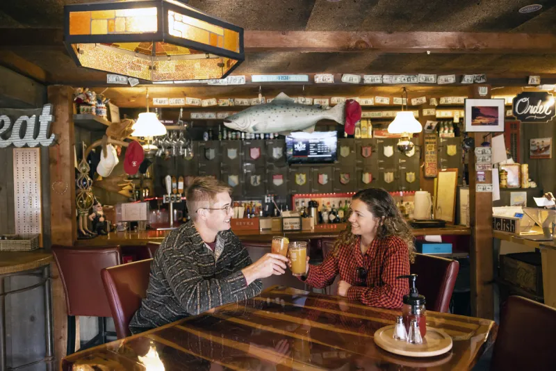 Young man and women cheers full beer pints at table in bar