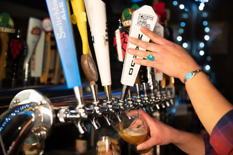 A close up of a woman's hand on a beer tap, which is dispensing golden beer into a glass.