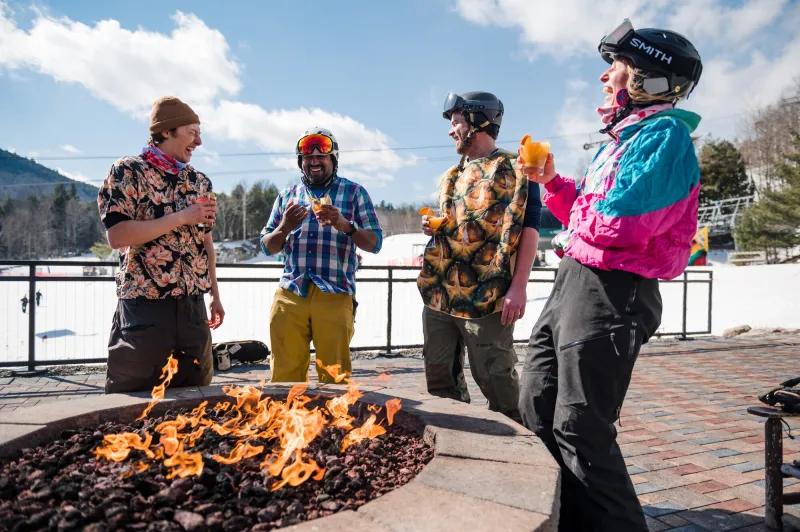 4 friends enjoy a drink around an open fire on the mountain