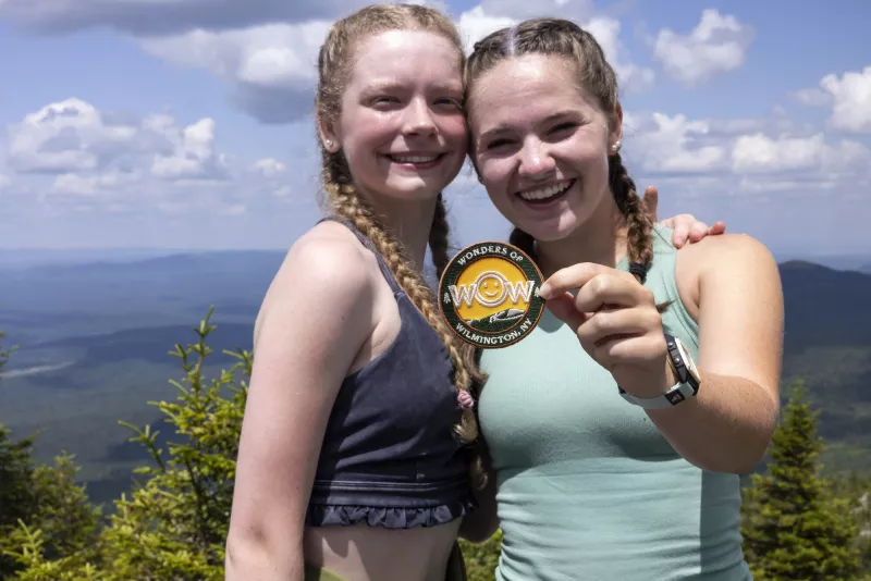 Two young people wearing braids in their hair smile as one holds a Wonders of Wilmington patch